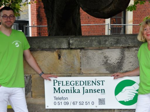 Fünf Personen in grünen T-Shirts und weißen Hosen halten ein Schild mit „Pflegedienst Monika Jansen" vor einem Baum.
